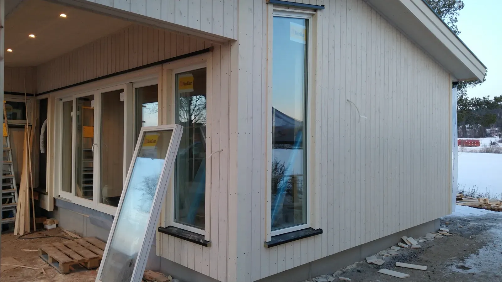 Ferdig tilbygg med ny hvit kledning og store vinduspartier — utsikt mot åpent landskap